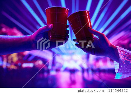 People having fun at nightclub, attending party, concert, drinking beer and clinking red cups with neon background 114544222