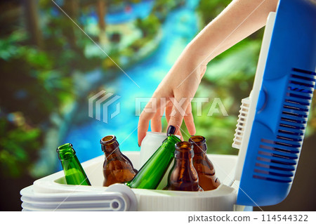Female hand grabs beer from cooler, perfect for a hot summer day. Picnic drinks, summer day outdoors Female hand grabs beer from cooler, perfect for a hot summer day. Picnic drinks, summer day outdoors 114544322
