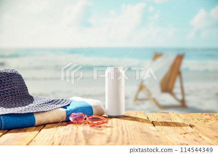 Beachside refreshment. Beer can bottle with hat and towel on beach with beautiful ocean view. Beachside refreshment. Beer can bottle with hat and towel on beach with beautiful ocean view. 114544349
