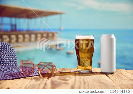 Chilling by the ocean. Frosty glass of beer with can on beachside table with beautiful ocean view background. Beach pub Chilling by the ocean. Frosty glass of beer with can on beachside table with beautiful ocean view background. Beach pub 114544380