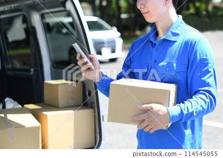 A male delivery driver holding a package and looking at his smartphone A male delivery driver holding a package and looking at his smartphone 114545055