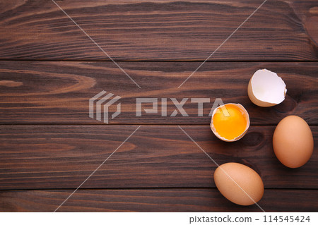 Chicken eggs and half with yolk on a brown background. 114545424