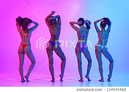 Rear view of young women, friends with slim, tanned bodies posing in swimwear in neon light against gradient background. 114545488