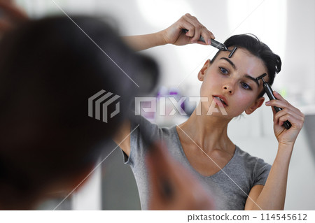 A young woman massages her face with gouache while looking in the mirror. 114545612