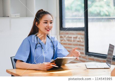 Smiling young female nurse reviewing patient chart at wooden desk in bright office. Smiling young female nurse reviewing patient chart at wooden desk in bright office. 114545995