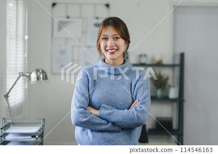 Smiling asian young woman standing by the window in a bright office environment. 114546163