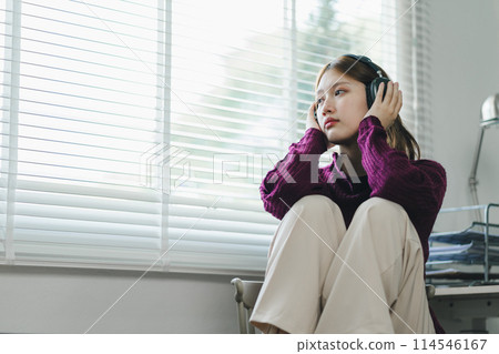 Depressed young woman with headphones sits in a chair and looking away at home. Depressed young woman with headphones sits in a chair and looking away at home. 114546167