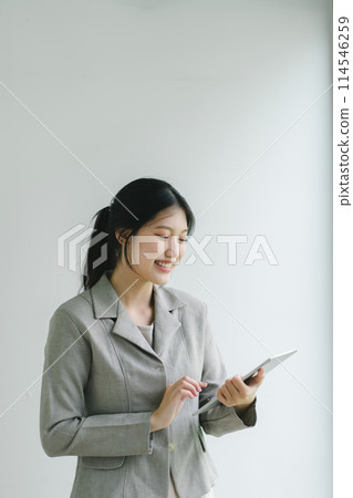 Confident Asian businesswoman smiling and using a digital tablet against a plain background. Confident Asian businesswoman smiling and using a digital tablet against a plain background. 114546259
