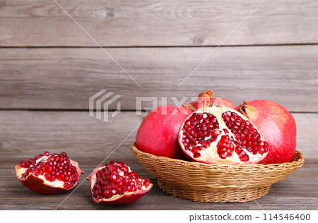 Ripe pomegranates on basket on grey wooden background 114546400