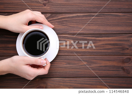 Female hands holding cup of coffee on brown wooden background. Female hands holding cup of coffee on brown wooden background. 114546848