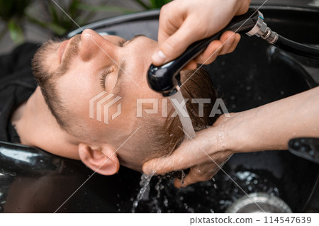 Skilled hairstylist tenderly rinses a clients hair with warm water in barbershop. Skilled hairstylist tenderly rinses a clients hair with warm water in barbershop. 114547639