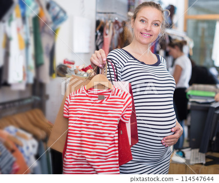 Pregnant woman in striped tunic chooses shirt in clothing shop 114547644