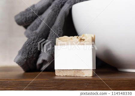 Soap bar with blank label near grey towel on basin on wooden countertop in bath, mockup Soap bar with blank label near grey towel on basin on wooden countertop in bath, mockup 114548330