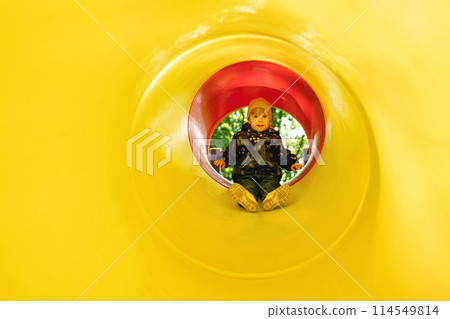 Active little girl inside a tube slide on playground. Cute little girl sliding down on slide. Healthy activity for children. Child on yellow background with free space for text. Childhood concept. Active little girl inside a tube slide on playground. Cute little girl sliding down on slide. Healthy activity for children. Child on yellow background with free space for text. Childhood concept. 114549814