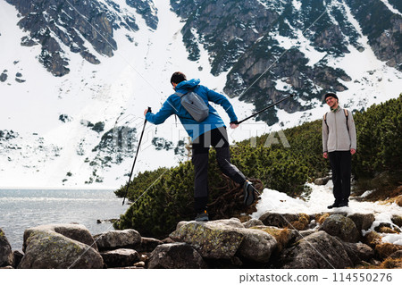 Two hikers explore snowcapped mountains and serene lake and have fun Two hikers explore snowcapped mountains and serene lake and have fun 114550276