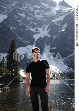Man in black shirt and sunglasses by lake with mountain backdrop 114550279