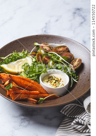 Vegan salad bowl with baked sweet potato, tomatoes, nuts, tahini dressing and sprouts, white background, top view. Vegan salad bowl with baked sweet potato, tomatoes, nuts, tahini dressing and sprouts, white background, top view. 114550722
