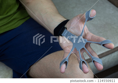 Finger trainer in stretched position while performing an exercise to develop hand and finger strength 114550911