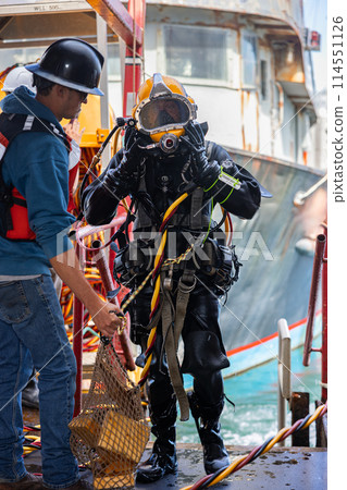 Tender assists commercial diver with helmet 114551126