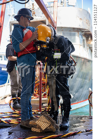 Tender assists commercial diver with helmet 114551127