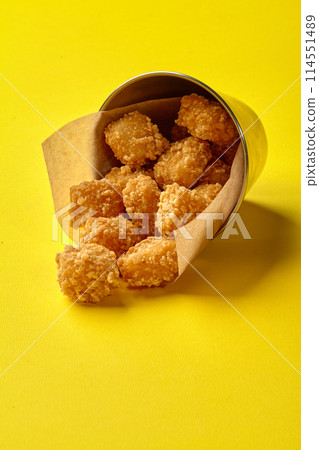 Crispy fried chicken nuggets spilling from metal bucket on yellow Crispy fried chicken nuggets spilling from metal bucket on yellow 114551489