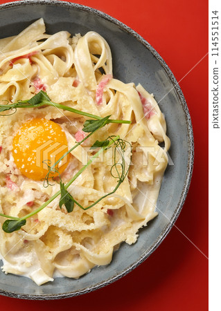 Fettuccine carbonara with pancetta, egg yolk and parmesan on red 114551514