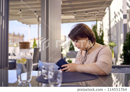 plus size woman in peach fuzz dress chooses a dish in a restaurant via QR code in smartphone, water with lemon and glasses in front of her plus size woman in peach fuzz dress chooses a dish in a restaurant via QR code in smartphone, water with lemon and glasses in front of her 114551764