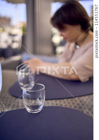 plus size woman in peach fuzz dress chooses a dish in a restaurant via QR code in smartphone, water with lemon and glasses in front of her 114551767