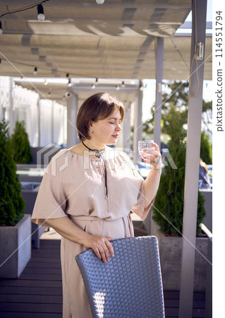 medium sized woman in peach fuzz dress with glass of water in restaurant 114551794