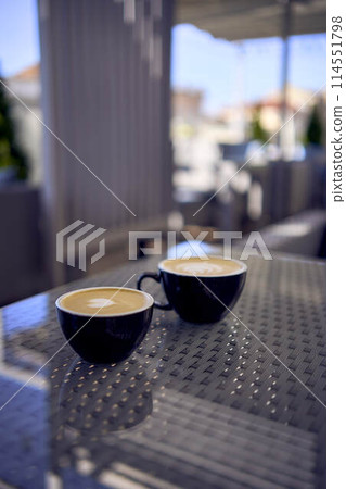 two cups of coffee, latte and cappuccino on a table in a cafe two cups of coffee, latte and cappuccino on a table in a cafe 114551798