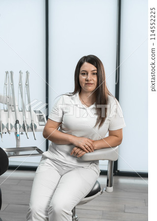 With an expression of care and aesthetics, the dentist demonstrates her beauty, creating a harmonious atmosphere in the office. The expression in her eyes conveys a desire to help patients achieve 114552225