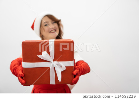 A smiling woman in red with a beautifully decorated gift in her hands creates a festive mood around for the new year and tears. Winter gift holidays are perfect for festive celebrations. 114552229