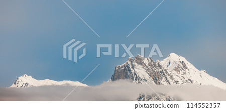 Snow-capped mountain peaks with clouds and clear sky 114552357