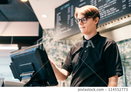 Young waiter serving customer at cash point in cafe. Man working with POS terminal. Cashier, barista checking for payment receipt. Hospitality, server and preparing a slip at the till in coffee shop 114552773