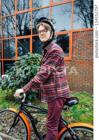 Young stylish man in helmet riding on cruiser city Bicycle on urban sidewalk to the office. Student on way to college on bike. Eco friendly transportation for carbon footprint. Sustainable lifestyle. 114552797
