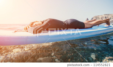 Woman sup yoga. Happy sporty woman practising yoga pilates on paddle sup surfboard. Female stretching doing workout on sea water. Modern individual female hipster outdoor summer sport activity. Woman sup yoga. Happy sporty woman practising yoga pilates on paddle sup surfboard. Female stretching doing workout on sea water. Modern individual female hipster outdoor summer sport activity. 114552821