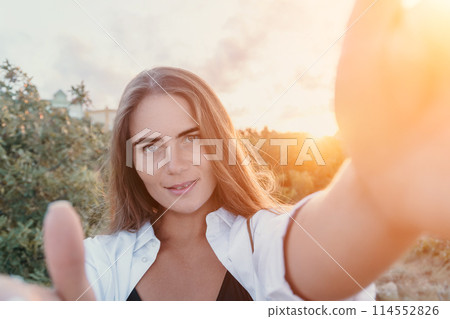 Amber Golden Hour Close up of a woman bathed in golden hour light making selfie on sunset in summer park. Happy tourist enjoy taking selfie photo outdoors for memories Amber Golden Hour Close up of a woman bathed in golden hour light making selfie on sunset in summer park. Happy tourist enjoy taking selfie photo outdoors for memories 114552826