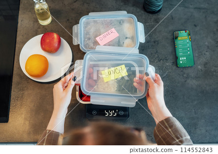 Healthy diet plan for weight loss, daily ready meal menu. Close up Woman weighing lunch box cooked in advance,ready to eat on kitchen scale. Balanced portion with healthy dish. Pre-cooking concept Healthy diet plan for weight loss, daily ready meal menu. Close up Woman weighing lunch box cooked in advance,ready to eat on kitchen scale. Balanced portion with healthy dish. Pre-cooking concept 114552843
