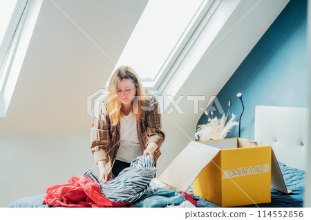Woman selecting clothes from her wardrobe for recycling, donating to a Charity shop. Decluttering, Sorting clothes, Cleaning Up. Reuse, second hand concept. Conscious consumer, sustainable lifestyle. Woman selecting clothes from her wardrobe for recycling, donating to a Charity shop. Decluttering, Sorting clothes, Cleaning Up. Reuse, second hand concept. Conscious consumer, sustainable lifestyle. 114552856