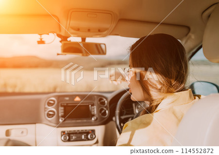 A woman in a yellow shirt is driving a car. She is wearing glasses and has her hands on the steering wheel A woman in a yellow shirt is driving a car. She is wearing glasses and has her hands on the steering wheel 114552872