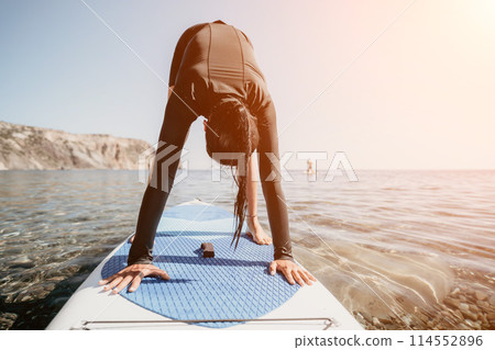 Woman sup yoga. Happy sporty woman practising yoga pilates on paddle sup surfboard. Female stretching doing workout on sea water. Modern individual female hipster outdoor summer sport activity. Woman sup yoga. Happy sporty woman practising yoga pilates on paddle sup surfboard. Female stretching doing workout on sea water. Modern individual female hipster outdoor summer sport activity. 114552896
