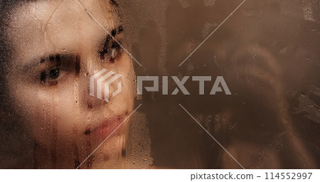 Woman touching steamy shower glass with hand Woman touching steamy shower glass with hand 114552997