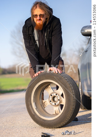 Man holding spare tire at roadside pitstop 114553066