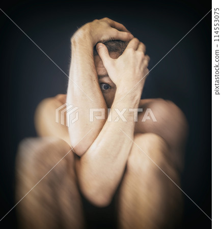 Man sitting in fear covering his face 114553075