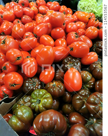 Farm products for healthy nutrition and vegetarians, vegetables - tomatoes of different varieties, sizes, red and green colors are on the counter in the grocery store among other plants and crops 114553567