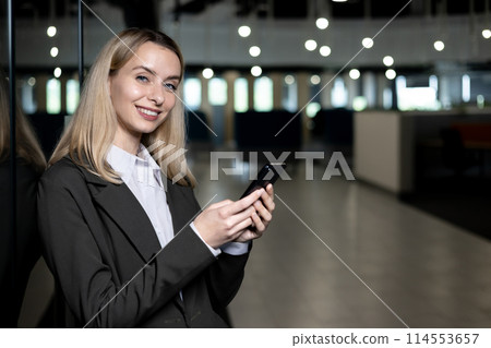 Smiling businesswoman holding and using smartphone in a modern, well-lit office space, representing communication and professionalism. Smiling businesswoman holding and using smartphone in a modern, well-lit office space, representing communication and professionalism. 114553657