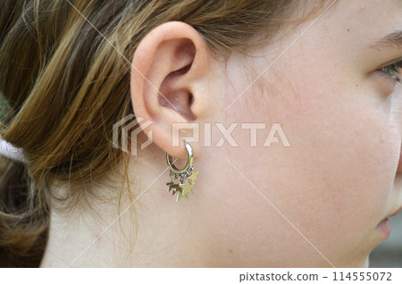A silver earring in the shape of small stars in the ear of a young girl 114555072