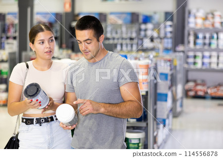 Positive young couple talking and looking for paints in store Positive young couple talking and looking for paints in store 114556878