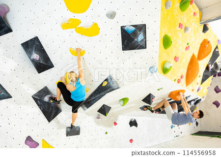 Woman and man alpinists practicing in pair indoor rock-climbing on climbing wall 114556958
