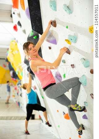 Young cheerful positive sporty woman training at bouldering gym without special climbing equipment 114557011